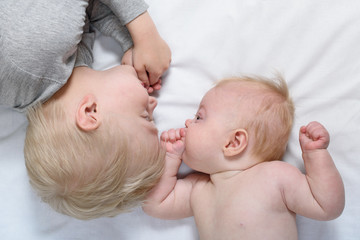 Baby and smiling older brother are lying on the bed. Funny and interact. Top view