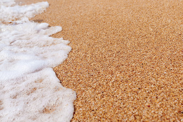 Fototapeta na wymiar closeup sea soft waves and foam on a sandy sea beach, summer sea and travel copyspace background