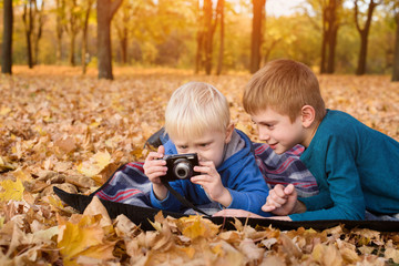 Two little brothers look at pictures on the camera. Lying in yellow autumn leaves. Fall day