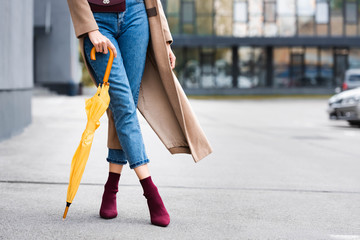 cropped view of woman in jeans holding yellow umbrella