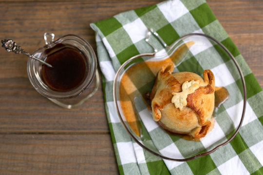 Freshly Baked Homemade Apple Dumplings in Apple Shaped Plate with Green and White Checked Napkin on Wooden Table; Apple Shaped Bowl of Brown Sugar Cinnamon Syrup in Background