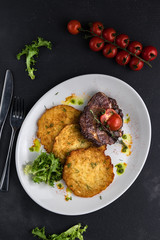 Top view Pork steak with pancakes with herbs and cherry tomatoes on a dark gray cement background