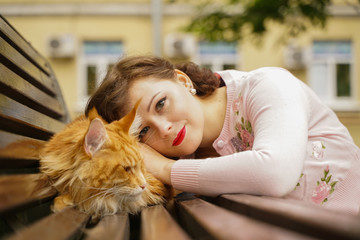 Fototapeta na wymiar big red maine coon cat is scary and sad. young owner woman hugs and strokes her orange pet in stress from first walk outdoor.