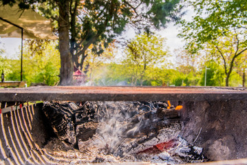 Chopped wood burns and smokes in the grill. Preparing for meat roasting on the fire. Barbecue in nature. Grill with smoke over summer outdoor nature in garden or park, outdoor, close up