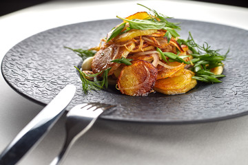 Fried potatoes with garlic and herbs on a black plate on a white background