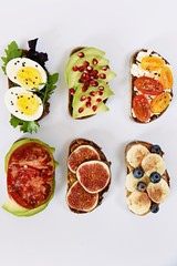 Six different toasts on the white background. Assorted toasts with eggs, fruits and berries, avocado and tomatoes.
