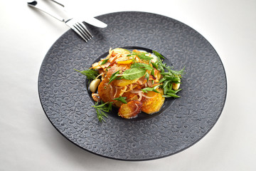 Fried potatoes with garlic and herbs on a black plate on a white background