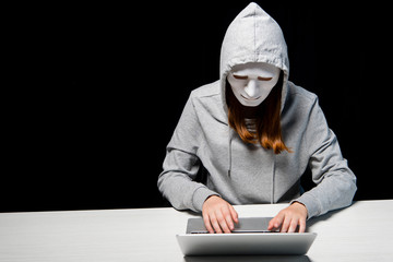 anonymous internet troll in mask typing on laptop keyboard isolated on black