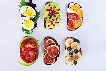 Six different toasts on the white background. Assorted toasts with eggs, fruits and berries, avocado and tomatoes.