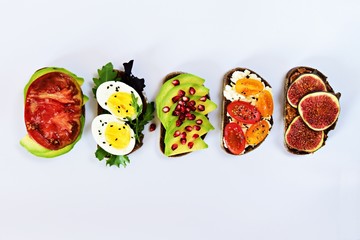Six different toasts on the white background. Assorted toasts with eggs, fruits and berries, avocado and tomatoes.
