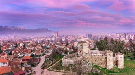Colorful, magenta, sunset sky over misty cityscape panorama and foreground ancient fortress in Pirot, Serbia