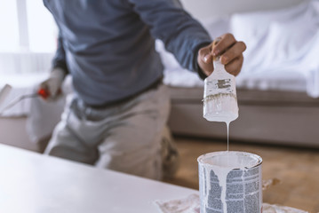 Color brush with paint pot. Hand holding the paint brush and bucket with white color on wood....