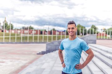 Handsome muscular athlete man smiles, looks carefully, close-up happy rejoices coach, summer city, sports shirt motivation youth lifestyle outdoor training. Motivation lifestyle. Free space for text.