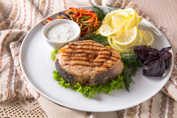 Grilled seabass, mullet, or dorado. Juicy delicacy fish on a plate with a salad of fried vegetables. Balkan cuisine. Restaurant menu
