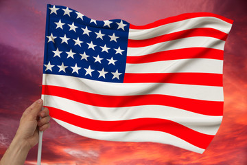 Fototapeta premium male hand holds the national flag of the USA on a luxurious texture of satin, silk with waves, closeup, copy space