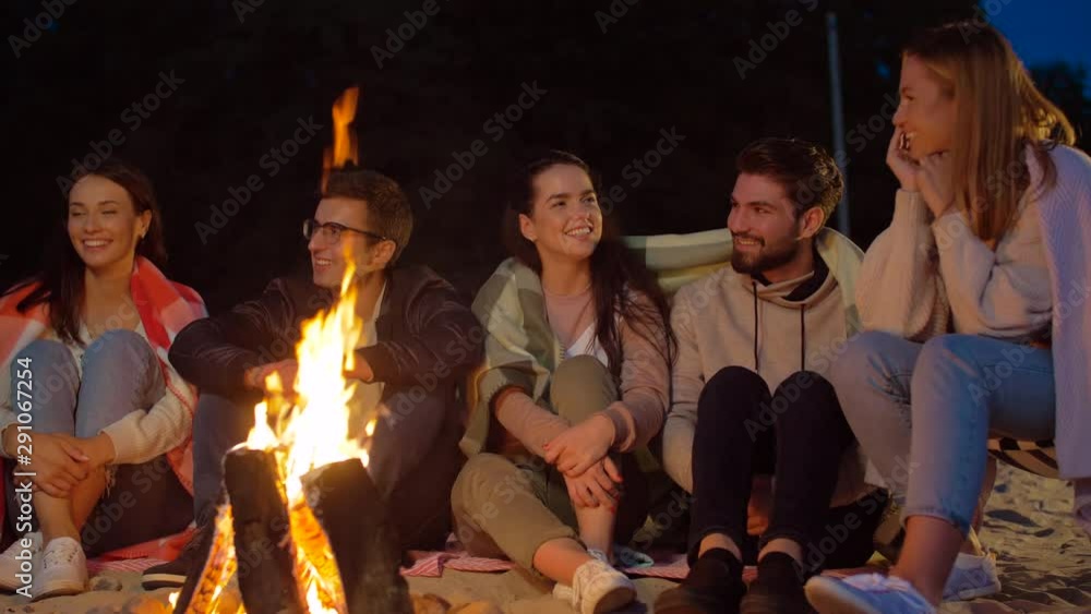 Sticker leisure and people concept - group of smiling friends sitting at camp fire on beach at night