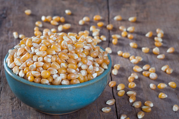 Dry corn kernels in a green bowl, set on a wooden table.