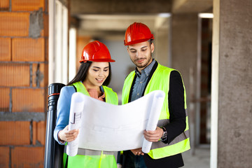 construction site engineers with blueprints wearing hard hats