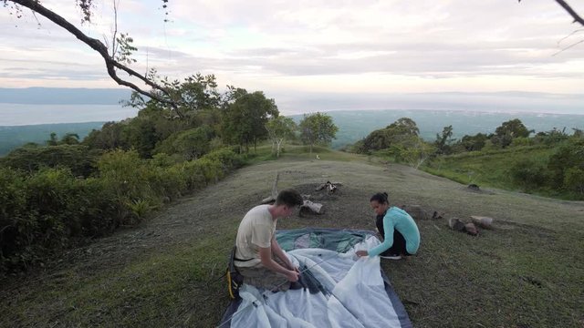 Couple setting up a tent in a campsite in the mountain with higland view.