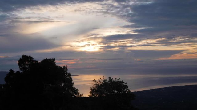 Timelapse of sunrise with colorful sky and clouds, ocean, trees and mountain.