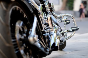 low angle of black rear tire and shiny silver steel gear of motorbike. Blur background