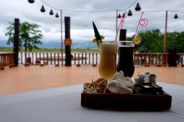 close up to glass of fruit juice and fried snacks on white tablecloth. Defocused terrace and cloudy sky background. At Inle lake Myanmar
