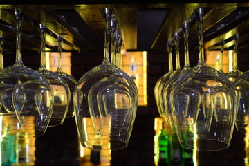  upside down wine glasses on bar counter. Blurred bottles of wine on cabinet as background