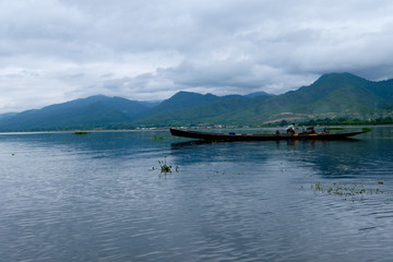 one fishing boat on rippled Inle lake. White cloudy sky with mountains. In Shan State Myanmar