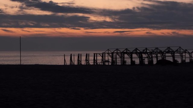 Beach hut frames in silhouette at dusk, against vivid sunset sky. Pan up
