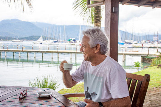 Senior man sitting drinking coffee by the sea enjoying the spot - Powered by Adobe