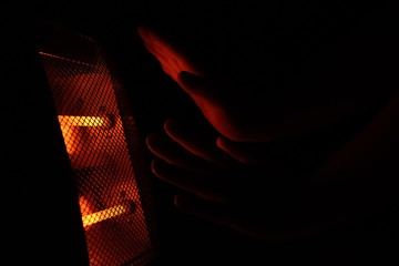 man warming up his hands with an electric heater in a very dark space