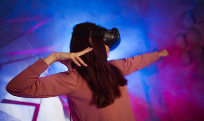 A young woman in virtual reality glasses, raised her hands in a combat pose. Shoots from an imaginary bow.