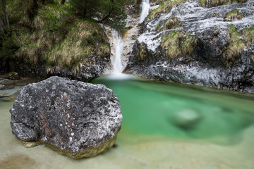 Alpine environment with a boulder in the foreground, and a small waterfall flowing into an emerald pond in the background © Roberto