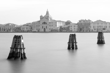 Paysage urbain noir et blanc de Venise, avec une ancienne église baroque surplombant l& 39 eau, avec trois groupes de pôles d& 39 amarrage en premier plan