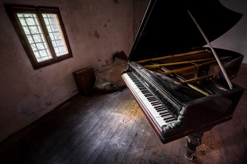 Wide angle shot of an ancient grand piano in an old abandoned house, with the floor made of weathered wooden boards