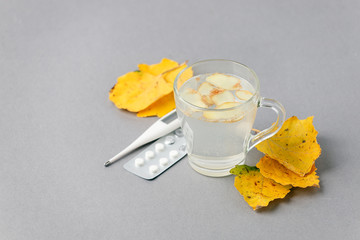 Food and drink, still life health care concept. Ginger tea infusion beverage in glass cup, yellow leaves, thermometer, pills on table, cold flu winter autumn days. Copy space