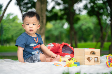 Toddler baby boy sitting in city green park playing toy