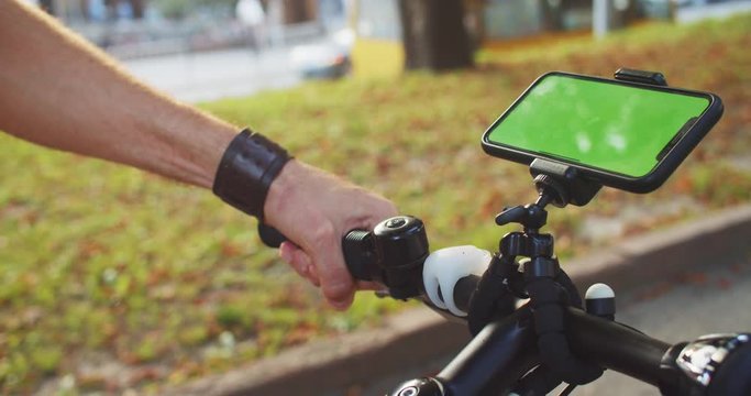 Mock-up greenscreen smartphone attached to bicycle handlebar. Close-up man riding a bike and using mobile phone application outdoor.