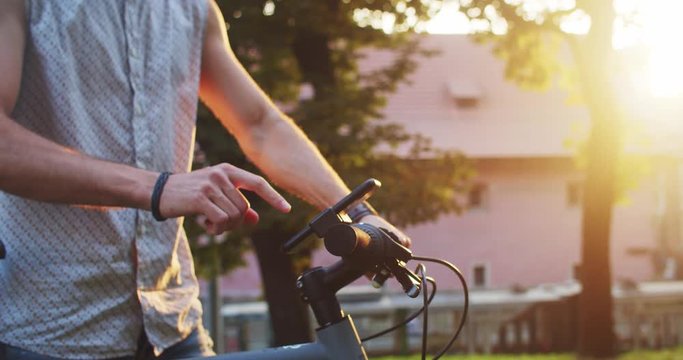 Modern male cyclist using smartphone activity tracker app mount on black mountain bike riding in the city on summer evening. Close-up.