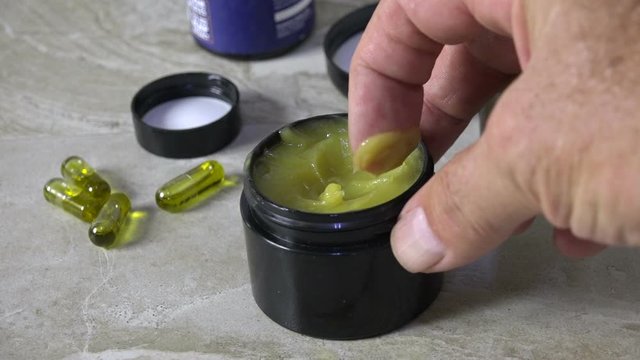 Closeup of a finger scooping CBD ointment from a jar