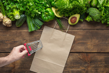 Paper bag with green vegetables and small shopping cart. Purchase Healthy vegan and vegetarian food