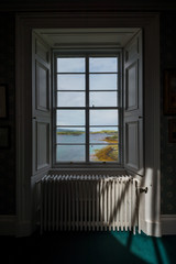 Interior of an old and elegant scottish house, with a window overlooking the coastline and distant islands 