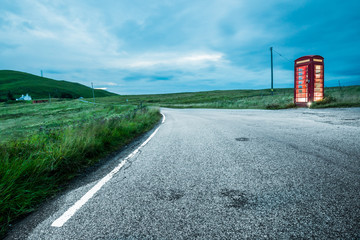 On a rural scottish road at night, lies a curbside solitary british red telephone booth