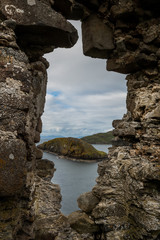 Through an opening on a rock wall can be seen the sea and a small island