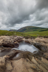 The scottish landscape of the Fairy Pools rapids, surrounded by green hills and under a cloudy sky
