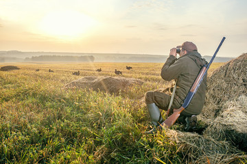 The man is on the hunt. Hunting period, autumn season. Male with a gun and binoculars at dawn. Hant...
