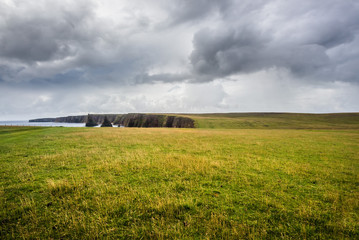 A lonely scottish landscape with the Duncansby Stacks in the distance, under a cloudy sky in a late afternoon summer day