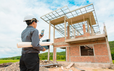 Asian manager of engineer architect in white helmet safety on construction site standing check a plan and project and take photo on smartphone