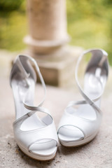 Close up of a pair of white high-heels wedding shoes lying on a balcony against a bokeh background