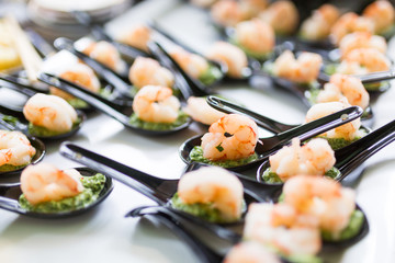 Close up of a tray holding a number of black chinese spoons each with a shrimp and some green dressing